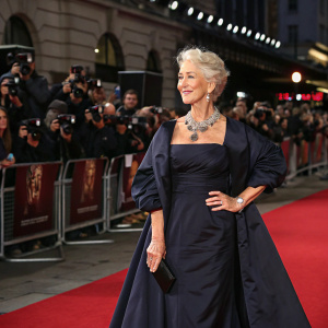 Helen Mirren at the UK TV Premiere for 'Catherine the Great'. She stands confidently in a black, elegant evening gown. Surrounded by a bustling crowd of photographers and fans in front of the iconic red carpet setup.