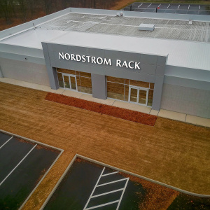 Aerial view of a modern Nordstrom Rack store. Large, clear signage visible from above. Gray and sleek architecture.