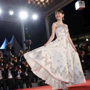 Park Eun-Ji, South Korean actress, at Cannes Film Festival. She is wearing a white dress with silver embellishments and a flared skirt. On stage with bright lights and a sea of photographers.