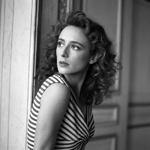 Black and white photo of actress Odile Le Clezio. Serious expression, curly hair. Striped dress, indoor setting.