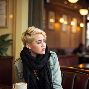 Miley Cyrus, blonde, short hair, in a cozy cafe. Wearing black scarf and casual jacket. Background is warm and inviting