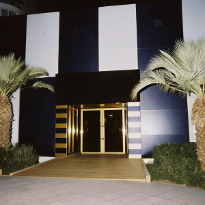 Modern nightclub exterior, Aura Club Kemer. Luxurious black and gold design. Palm trees and greenery surrounding the entrance.
