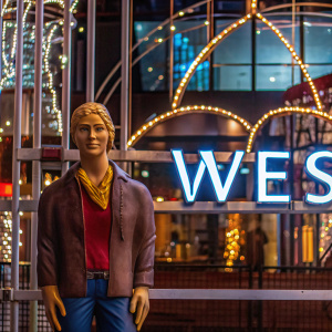 A digital avatar from Amazon Sumerian, with serene expression, blonde hair, and casual clothing. Set against bright white backdrop, showcasing WES text