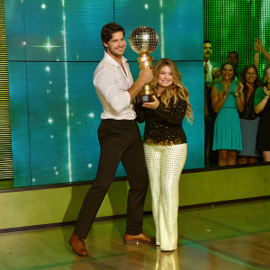 Gleb Savchenko and Sasha Pieterse, smiling, on stage at 'Dancing with the Stars' finale. Crowd cheering