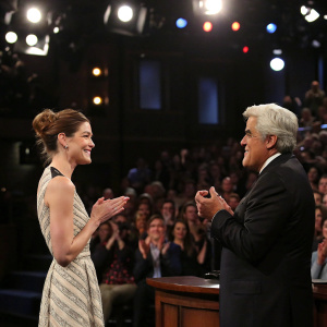 Michelle Monaghan, with a bun hairstyle, and Jay Leno at the opening monologue of The Tonight Show. Bright studio lights, audience applause