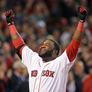 Photo of David Ortiz celebrating after a victory. African American man with close-cropped beard, white jersey with red accents, Boston Red Sox logo. Arms raised high, crowd blurred