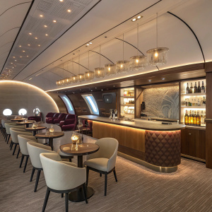 A sleek and sophisticated lounge bar aboard the Qatar Airways A380. Modern chairs, ambient lighting, bottles on the bar counter, curved ceiling, pendant lights, warm ambiance, Qatar branding