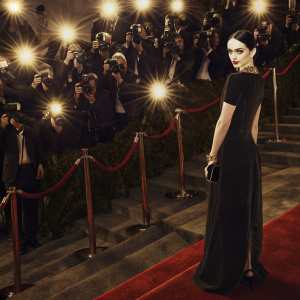 Krysten Ritter, in a sleek black dress, at the Met Gala. Eye-catching makeup and bold jewelry. Crowded and glamorous red carpet backdrop.