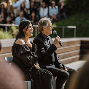 Phoebe Cates and Kevin Kline during a Q&A session at Cannes Film Festival. Phoebe in black dress with ruffled detail and shoulder accent, Kevin in dark suit. Audience blurred in background