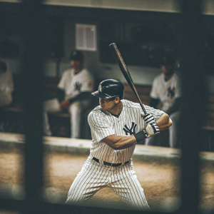 Aaron Judge, in Yankees uniform, intense batting stance at Yankee Stadium. Background shows blurred spectators and dugout.