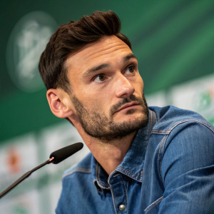 Close-up photo of Hugo Lloris. Denim shirt, intense gaze, blurred green background. Press conference