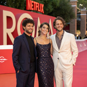 Carlos Peralta, Daniela Demesa, and Marco Graf attending the 'Roma' premiere. Dressed in elegant outfits on vibrant red carpet. Netflix logo backdrop