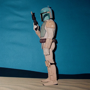 Digital illustration of Boba Fett from Star Wars. In a cartoon style with textured details, limited green and beige color palette. Standing in profile pose with his signature armor, helmet, gun, and gun holster against dark green backdrop.