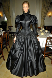 40 yo attractive lady wearing Victorian shiny black satin dress, very narrow waist and massive pushed up bosom. long puff sleeves, floor length big skirt with petticoat. sitting at dinner table.  