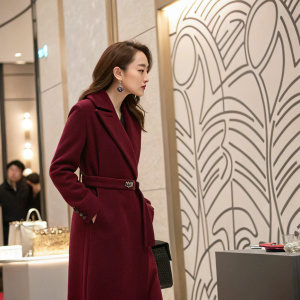 Dilraba Dilmurat at a luxury brand launch event. Wears a maroon overcoat, looking contemplative. Indoor setting, abstract patterned backdrop