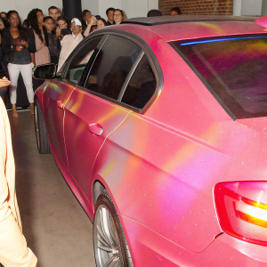 A sleek red BMW M3 parked at a bustling car show. Neon lights and enthusiastic crowds in the background.