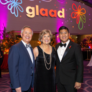 David Kopay, Joan Garry, and Esera Tuaolo at the annual GLAAD Awards. Formally dressed, standing in front of the GLAAD logo backdrop in a vibrant, colorful room.