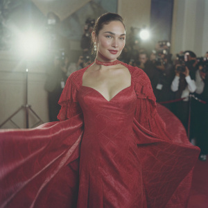 Gal Gadot at the Golden Globe Awards, dressed in an elaborate red velvet gown with a deep V-neckline. Stands confidently on the red carpet.