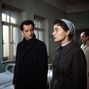 A 1958 Turkish film scene from 'Ögey Ana filmi'. Actors wearing dark clothes, standing in what appears to be a dimly lit room, possibly a hospital or home. Serious expressions on their faces. Natural lighting, somber mood.