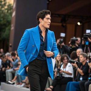 Cristiano Caccamo, dressed in a vibrant blue blazer and black slacks, addresses the crowd at a tech conference. A sea of cameras and attendees fill the background.