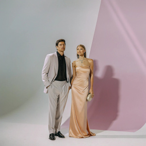 Formal event photo of Robert Lewandowski and Anna Lewandowska. Robert in black tailored tuxedo, dark styled hair. Anna in strapless, off-the-shoulder orange gown. Both posing for camera. Bold graphic backdrop