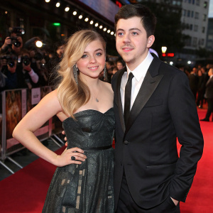 Chloe Grace Moretz and Christopher Mintz-Plasse at the premiere of a blockbuster film. They wear formal attire. The red carpet is bustling with fans and photographers.
