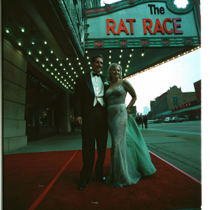 James Caan and Linda Stokes, dressed in elegant attire, at the Hollywood premiere of 'The Rat Race'. The event is held in a grand theater with red carpet and flashing lights.