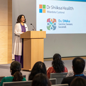 Dr. Shikha Sharma, wellness expert and founder of Dr. Shikha's Nutrihealth, giving a keynote speech at the Microsoft Teams summit. Conference hall with attendees in the background.