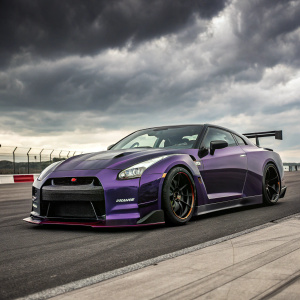 Midnight purple Nissan R35 GTR with black trim. Sleek, aggressive design due to wide body and large front air intake. Inspired by Nismo performance enhancements. Racing track setting.