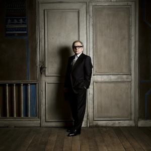 Martin Scorsese, in a dark suit and glasses, poses for a photograph at Cannes Film Festival. The backdrop features a deep blue wall adorned with various film festival logos.
