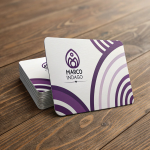 Business card for Marco Indago, white background with purple accents. Logo and contact info present. Part of a stack on wooden table