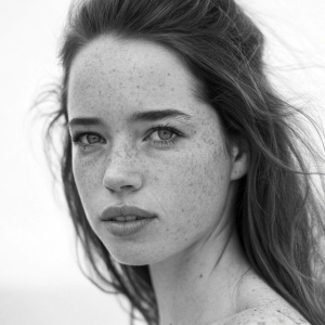 Anna Popplewell, with freckles and fair skin, serious expression. Black and white photo, minimalistic background