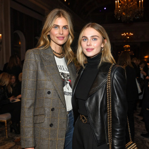 Donna Air and Freya Air Aspinall at a chic fashion gala. Donna in a tweed blazer and graphic tee. Freya in black leather jacket and turtleneck. Dimly lit ballroom with other attendees.