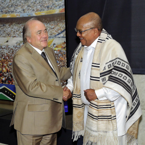 Sepp Blatter, the FIFA President, shaking hands with Jacob Zuma. A vibrant stadium backdrop with cheering fans and national flags