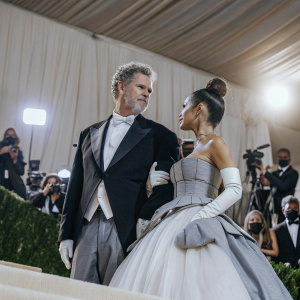 Will Ferrell and Ariana Grande at the MET Gala, dressed in elaborate gowns and tuxedos. Bright stage lights and paparazzi in the background.