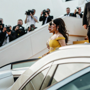 Salma Hayek at Cannes Film Festival. Wearing a vibrant yellow dress with intricate beadwork. Stands against a crowd scene with flashes