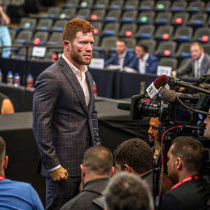Canelo Álvarez at a boxing press conference, with bruised knuckles and intense gaze.