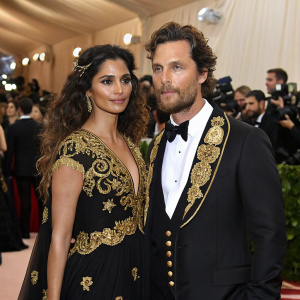 Matthew McConaughey and Camilla Alves attending the Met Gala. Dressed in black and gold evening wear. Crowded venue with celebrities and media.