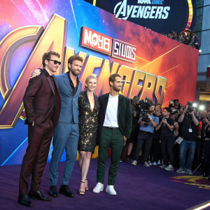 Avengers cast at Comic-Con. Bright, vibrant backdrop with Marvel logos. Fans and cameras in the background.