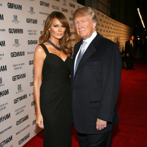 Formal photo of Melania Trump and Donald Trump at gala. Elegant black dress for Melania, dark suit for Donald. Red carpet, Gotham Magazine logos in background.