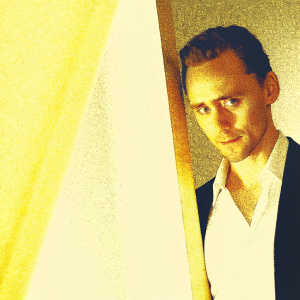 Tom Hiddleston, the charismatic actor, captures the essence of a magazine cover. Close-up shot highlighting his chiseled jawline and warm, engaging eyes. He is dressed in a classic white shirt and a sleek, black blazer. The dark, moody background accentuates the vibrant, splashes of orange that subtly highlight his figure.