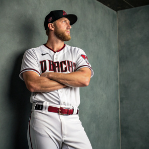 Portrait of Merrill Kelly, baseball star. Wearing Arizona Diamondbacks jersey. Gray backdrop, confident pose.