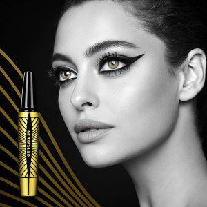 An advertisement for Maybelline's Colossal Kajal mascara featuring a woman with a dramatic eye look. Black background, minimalistic design.