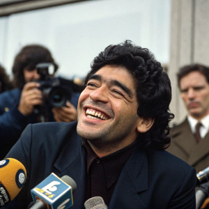 Diego Maradona in a candid moment at a press conference. Dark suit, joyful smile