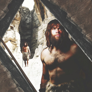 Digital art featuring a Neanderthal-like character from Far Cry Primal. He has a rugged, determined look with a dense beard. Set against a backdrop of rocky cliffs and other Neanderthals. Earthy color palette.