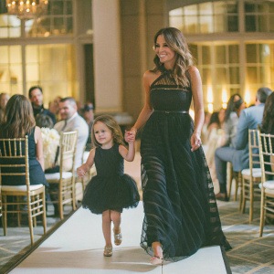 Brooke Burke-Charvet and her daughter Heaven Rain Charvet at the ChildFund Heroes Awards. Brooke is in a black, floor-length gown with intricate details, while Heaven Rain wears a matching mini-dress. Formal event setting with attendees in evening wear.