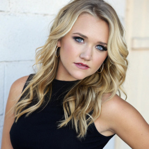 Close-up professional portrait of Emily Osment, a talented actress with wavy blonde hair and bright blue eyes. Caucasian, fair skin, neutral expression, subtle lip color. Posing confidently in a black cropped top against a simple, neutral backdrop.