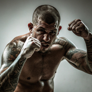 Close-up photo of UFC fighter Anthony Pettis. He's in fighting stance with visible muscles and tattoos. Plain white background