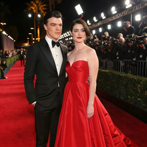 Finn Wittrock and Sarah Roberts at a glamorous Hollywood gala. They are dressed in exquisite evening wear against a backdrop of vibrant red carpet and flashing cameras.