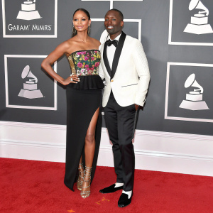 Alesha Dixon and Azuka Ononye at the 2017 Grammy Awards. Alesha in a black dress with vibrant bodice and high-waisted design. Azuka in a white suit with black vest. Crimson carpeted stage, backdrop with Grammy logo and sponsor logos